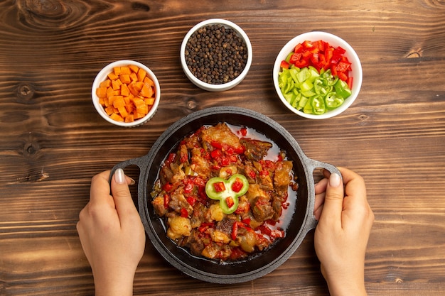 Top view cooked vegetable meal with seasonings and sliced pepper on the wooden brown desk