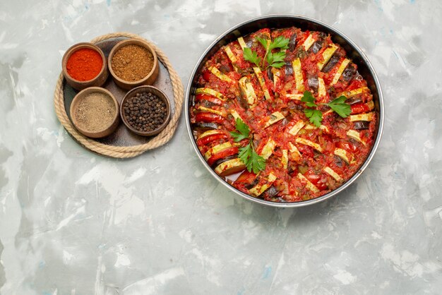 Top view cooked vegetables inside round pan along with seasonings on the bright background vegetable food meal dish dinner