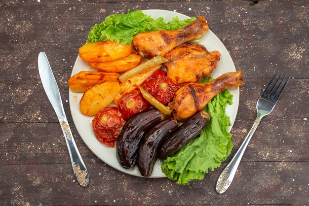 Top view cooked vegetables such as potatoes tomatoes and eggplants with meat inside white plate with salad on brown