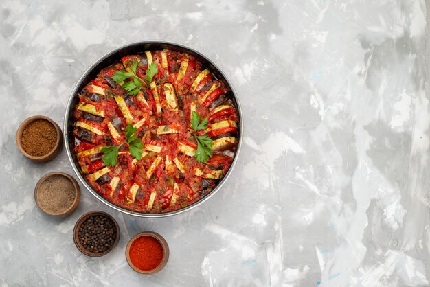 Top view cooked vegetables with greens and seasonings inside pan on the bright desk vegetable food meal dish