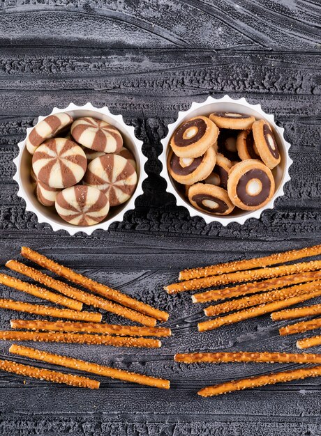 Top view of cookies in bowls and crackers on dark  vertical