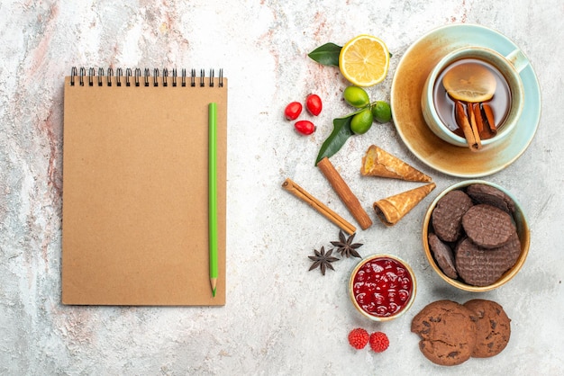 Top view cookies a cup of black tea with lemon cinnamon lemons jam star anise notebook and pencil