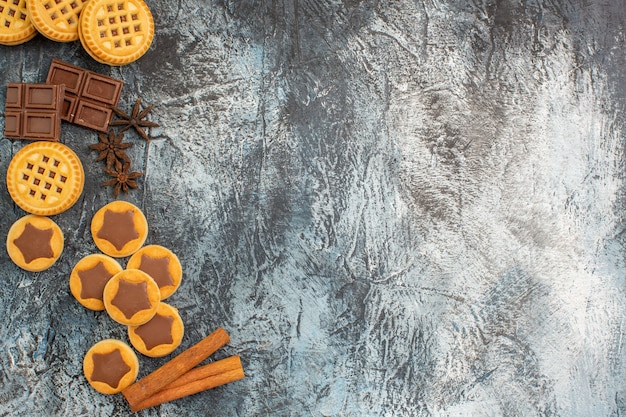 Free photo top view of cookies with cinnamon sticks and chocolates on the left side of grey ground