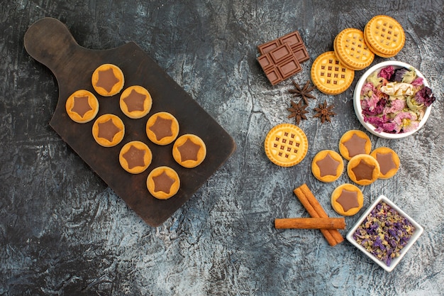 Top view of cookies on wooden platter and dry flowers on grey background