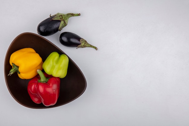 Top view  copy space eggplant with colored bell peppers in bowl on white background