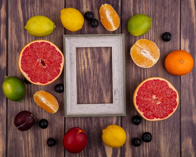 Free photo top view  copy space gray ball frame with peach  lemons  limes  orange and half grapefruit on wood background