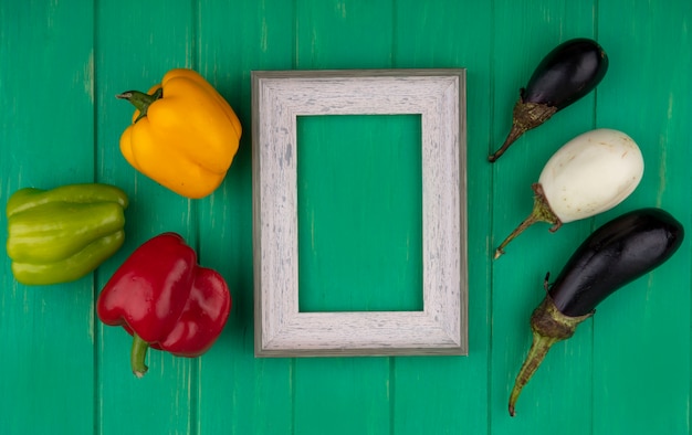 Top view  copy space gray frame with colored bell peppers  with white and black eggplants on a green background