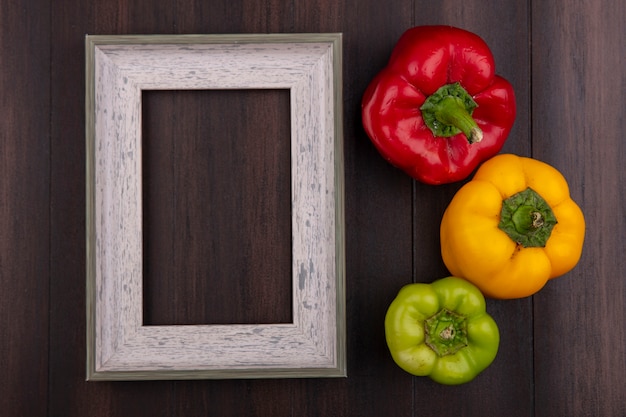 Top view  copy space gray frame with colored bell peppers on wooden background