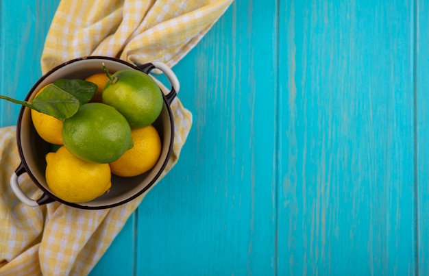 Top view  copy space lemons with lime in a saucepan and yellow checkered towel on turquoise background