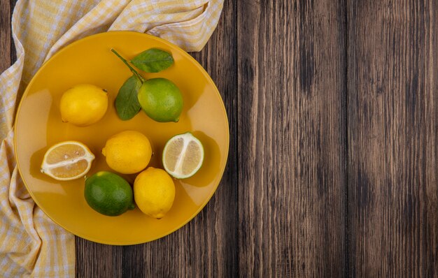 Top view  copy space lemons with limes on yellow plate with yellow checkered towel on wooden background