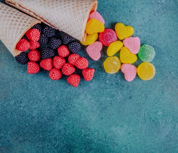 Free photo top view copy space marmalade in the shape of raspberries blackberries and hearts with waffle cones on a dark green background