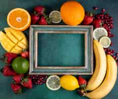 Free photo top view copy space mix of fruits mango banana strawberries lemon orange with frame on green