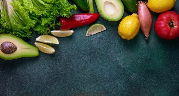 Top view copy space mix of vegetables avocado lemon red pepper onion and lettuce on a dark green background