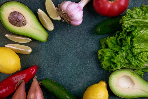 Top view copy space mix of vegetables avocado lemon tomato cucumbers and lettuce on a dark green background