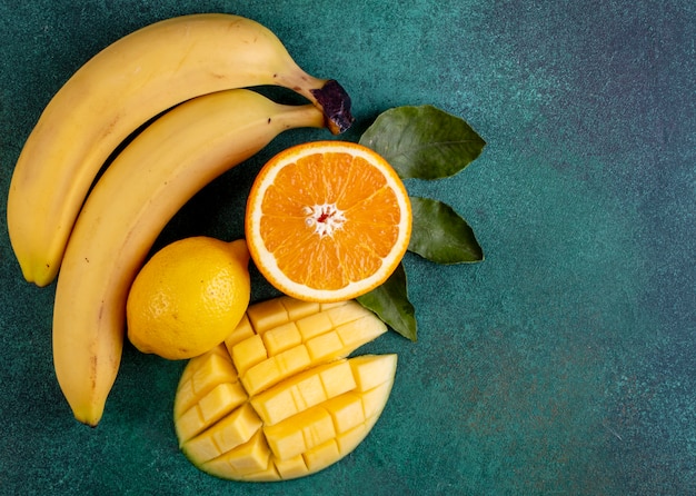 Free photo top view copy space sliced mango with bananas half an orange and lemon on green