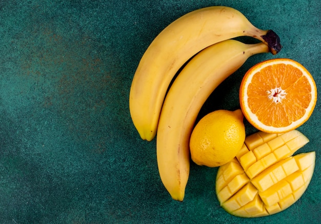 Top view copy space sliced mango with bananas half an orange and lemon on green