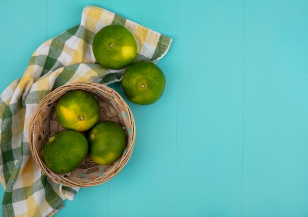 Top view copy space tangerines in basket with checkered towel on light blue wall