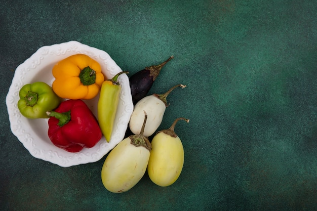 Top view  copy space white and black eggplant with bell peppers on a plate on a green background