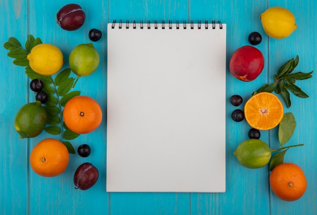 Top view  copy space white notepad with oranges  cherry plums  lemons  limes and plums on a turquoise background