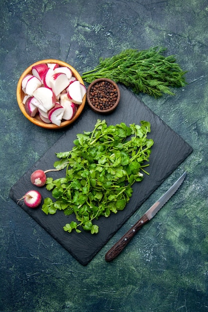 Free photo top view of coriander bundle fresh whole chopped radishes pepper on wooden cutting board and knife on green black mixed colors background with free space