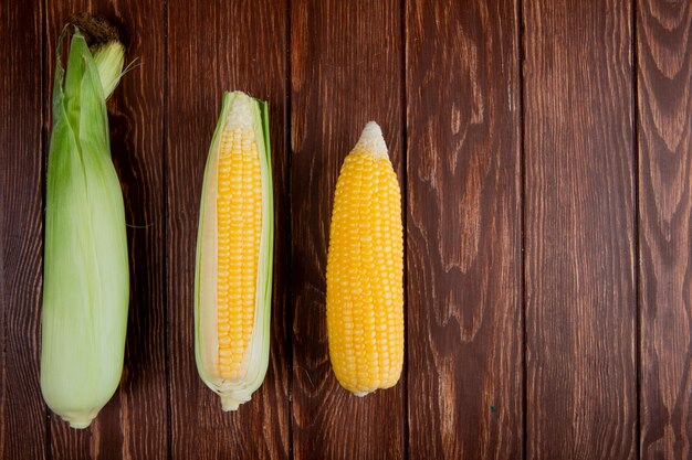 Top view of corn cobs with shell on left side and wooden surface with copy space