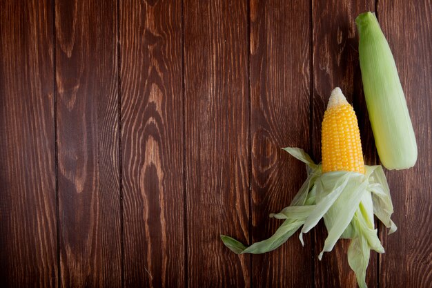 Top view of corn cobs with shell on wooden surface with copy space