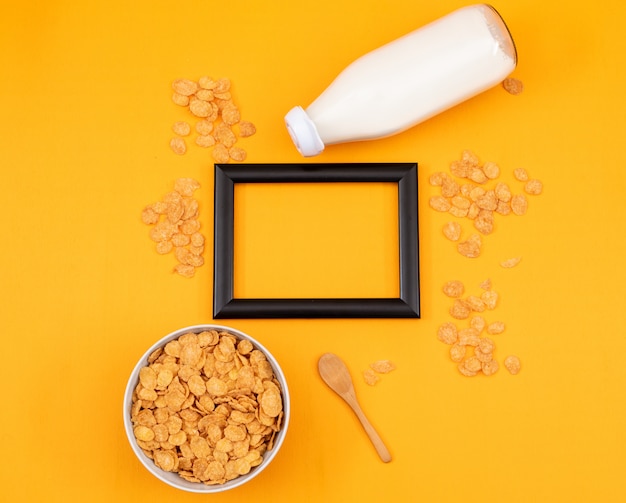 Free photo top view of cornflakes and milk with copy space in black frame and yellow background horizontal