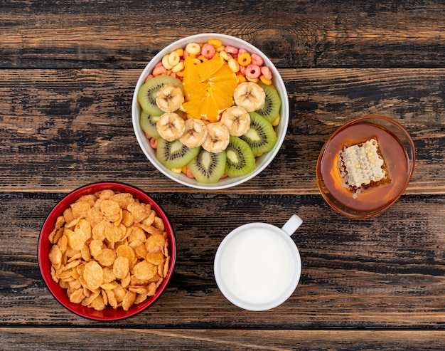 Top view of cornflakes with fruits and honey on dark wooden surface horizontal