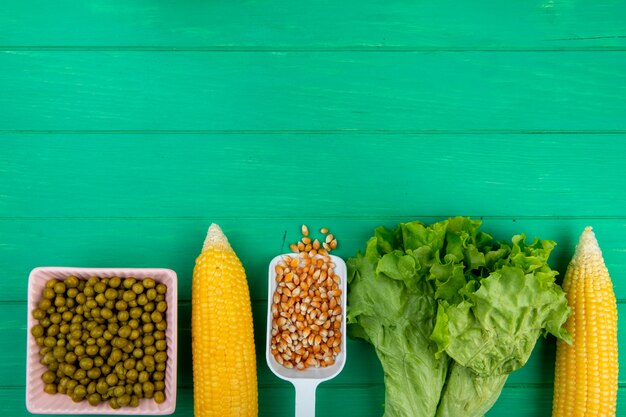 Top view of corns and corn seeds with green peas lettuce on green surface with copy space