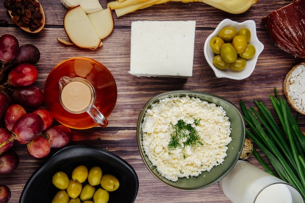 Free Photo top view of cottage cheese in a bowl with feta cheese  honey in a glass bottle sweet grapes and pickled olives on rustic wood