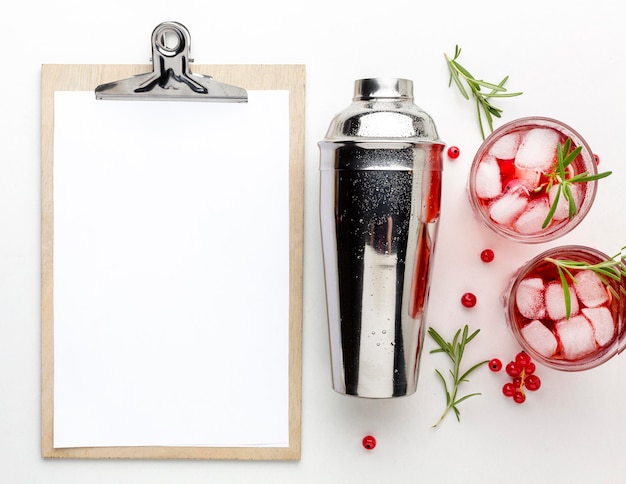 Free photo top view cranberry vodka glasses with shaker and blank clipboard