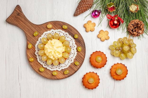 Top view cream cake with little sweet cakes and grapes on white desk fruit cookie cake biscuit pie