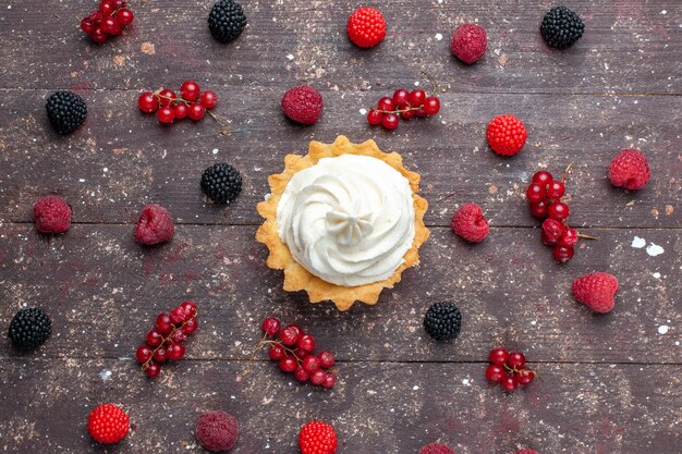 Top view of creamy delicious cake along with differented berries spread all over the brown desk, berry fruit cream bake biscuit