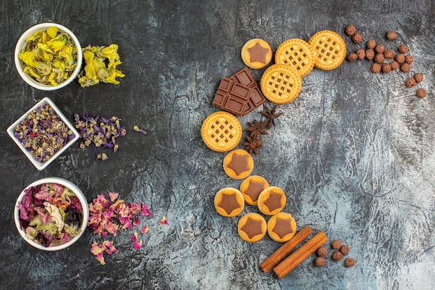 Top view of crescent shaped layout of sweets and bowls of dry flowers on grey ground