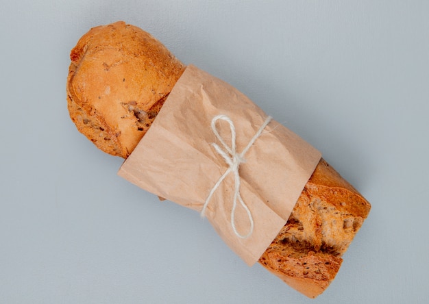 Top view of crispy baguette packed in paper on blue background