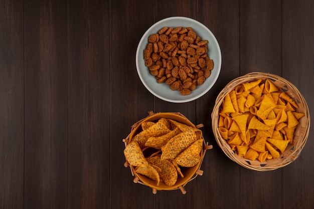 Free photo top view of crispy tasty rye rusks on a bowl with spicy chips on a bucket with corn snacks on a bucket on a wooden table with copy space