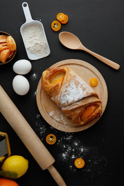 Free photo top view of croissant on trivet with egg flour kumquat lemon tangerine spoon and rolling pin on black background