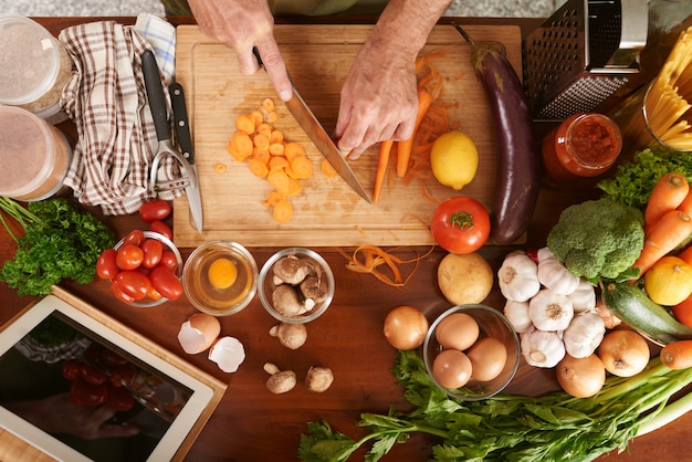 Top view of cropped hands of senior cook unrecognizable cutting carrot cooking vegetable stew