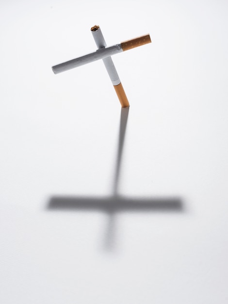 Free Photo top view of cross sign made from cigarette with it shadow on isolated on white background