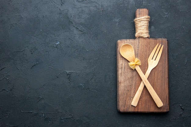 Free photo top view crossed wooden spoon and fork on wooden serving board on black table copy place