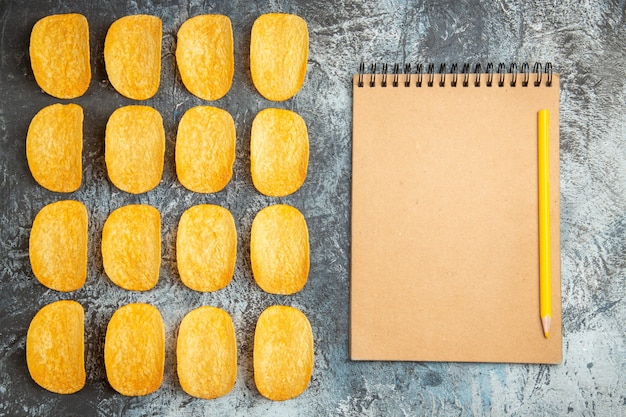 Free photo top view of crunchy baked five chips lined up in rows and notebook with pen on gray background