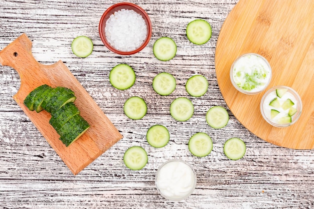 Free photo top view cucumber sliced with salt in bowl and yogurt on cutting board on white wooden