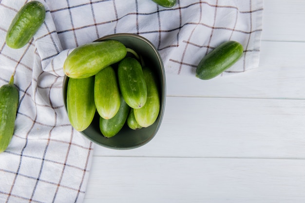 Free photo top view of cucumbers in bowl with other ones on plaid cloth and wood