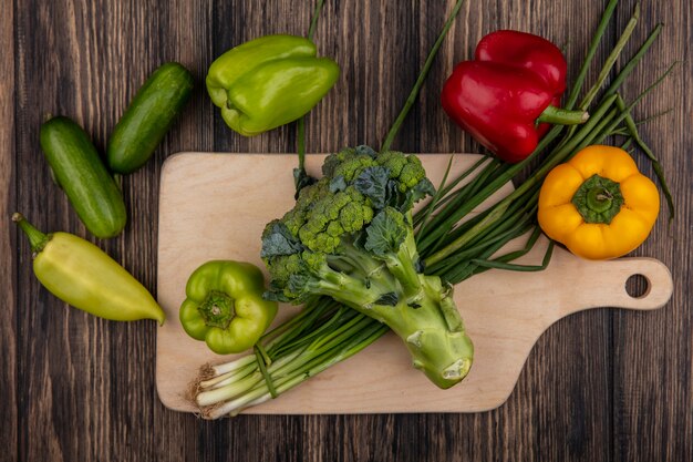 Top view cucumbers with green peppers  broccoli and green onions on a cutting board  on a wooden background