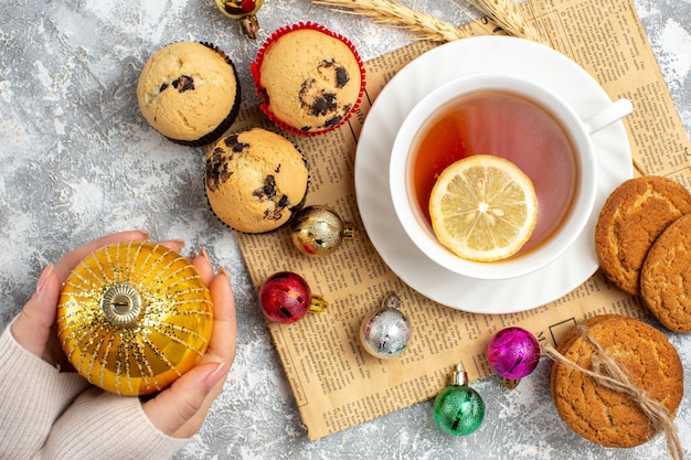 Top view of a cup of black tea and decoration accessories on an old newpaper cookies and small cupcakes on ice surface