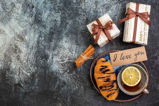 Top view of a cup of black tea delicious croisasant i love you writing on a tray cinnamon limes gifts on dark background