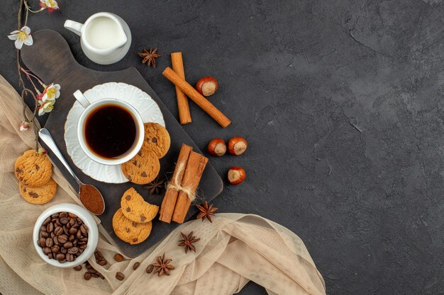 Top view cup of coffee anises cookies spoon on wood board coffee beans in bowl on dark surface