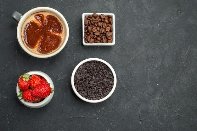 Free Photo top view a cup of coffee bowls with strawberries chocolate coffee seeds on dark background