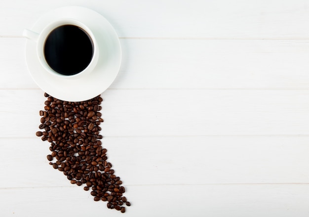 Top view of a cup of coffee and coffee beans scattered on white background with copy space