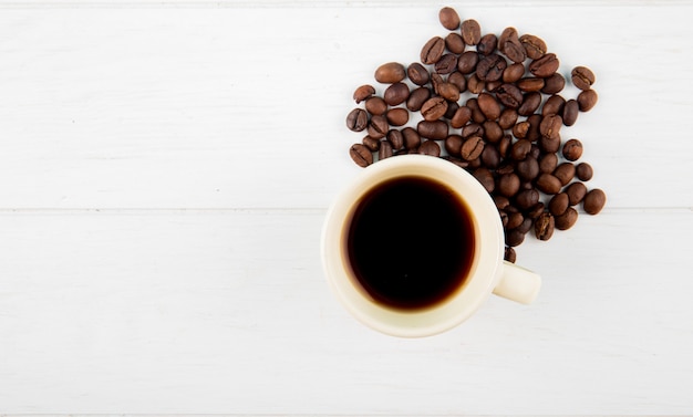 Top view of a cup of coffee and coffee beans scattered on white background with copy space